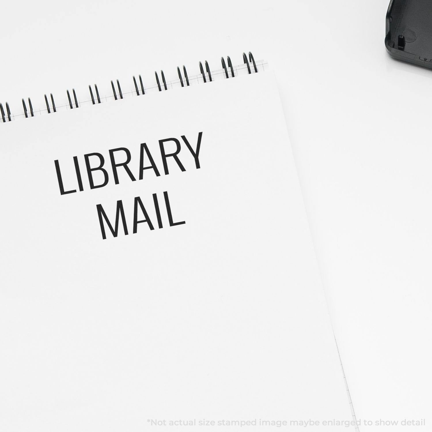 A Large Library Mail Rubber Stamp imprint on a white spiral notebook, with the text LIBRARY MAIL clearly visible.