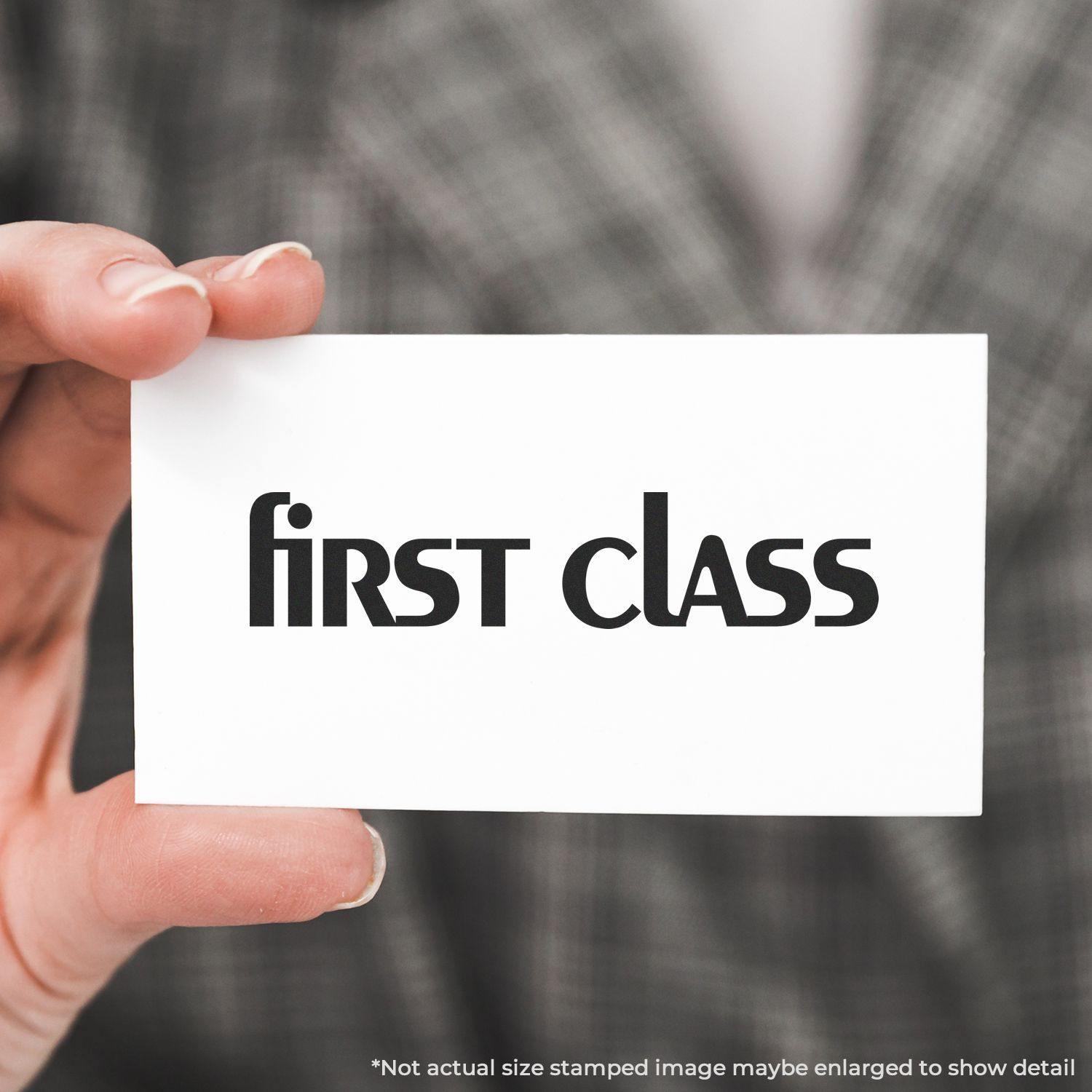 A hand holding a card stamped with first class using the Large Lower Case First Class Rubber Stamp. Background shows a blurred plaid jacket.