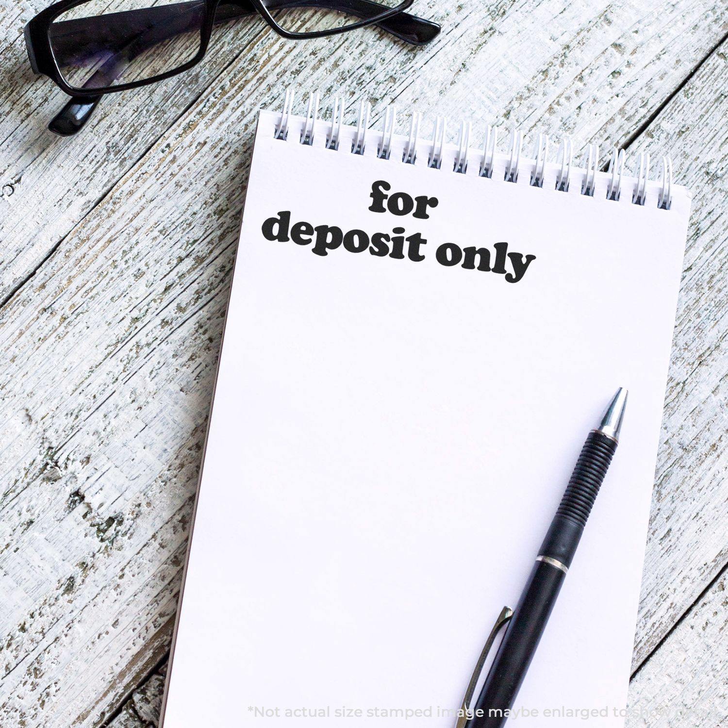 Large Self Inking Lowercase For Deposit Only Stamp used on a white notepad, with a pen and glasses placed nearby on a wooden surface.