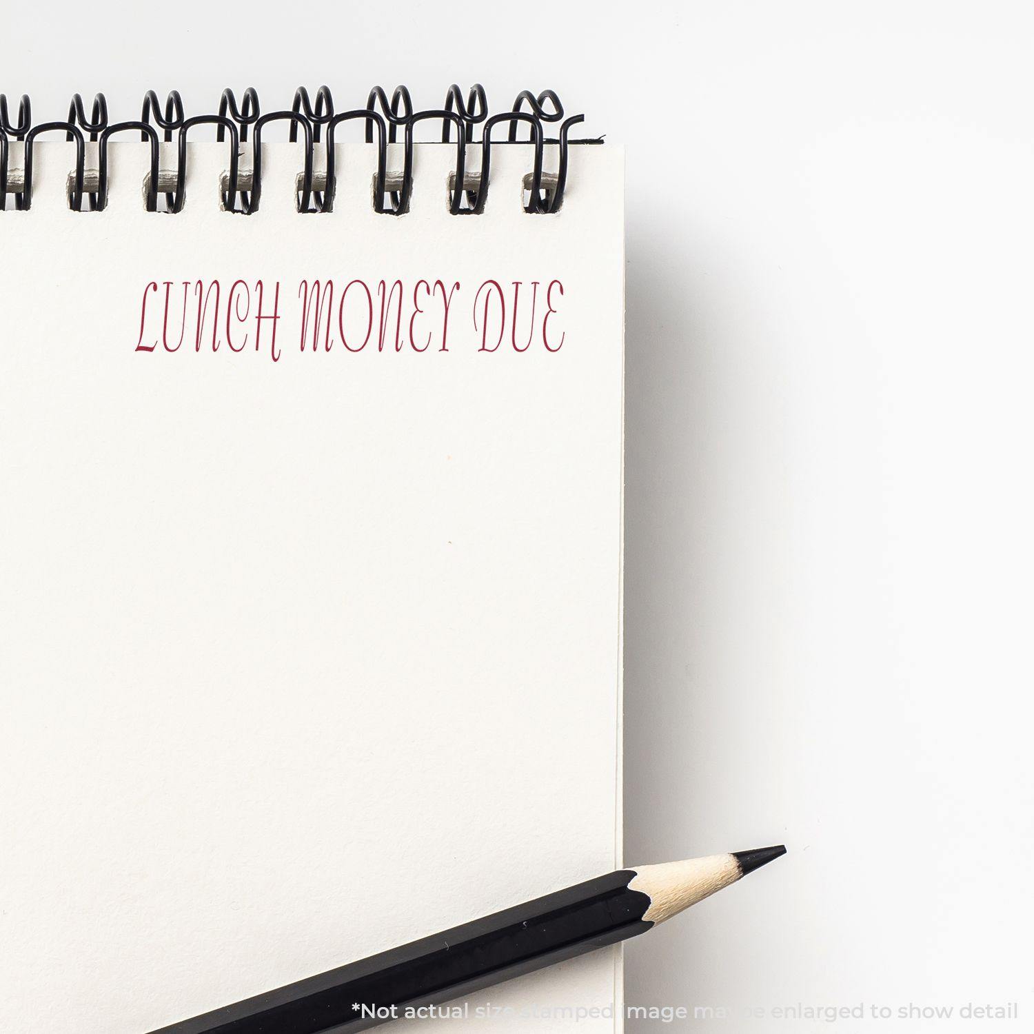 A notebook with LUNCH MONEY DUE stamped in red using the Large Lunch Money Due Rubber Stamp, with a pencil beside it.