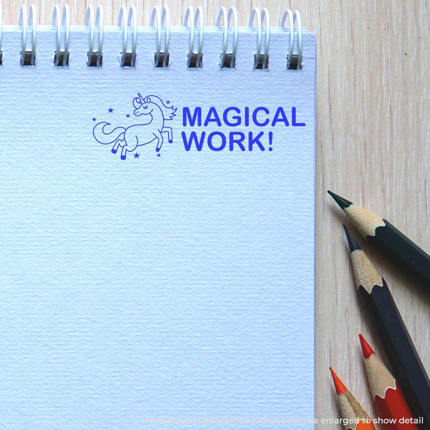 A notebook with a blue MAGICAL WORK! imprint from the Large Magical Work Rubber Stamp, next to colored pencils on a wooden surface.