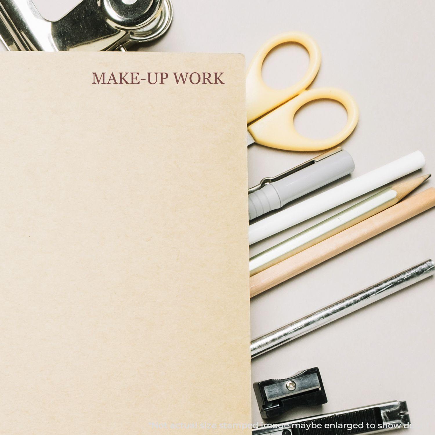 Large Pre-Inked Make-Up Work Stamp used on a brown folder, surrounded by stationery items like scissors, pens, pencils, and a clipboard.