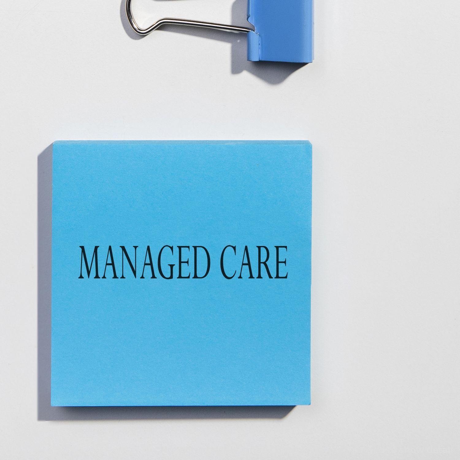 Large Self Inking Managed Care Stamp imprint on a blue paper with a blue binder clip on a white background.