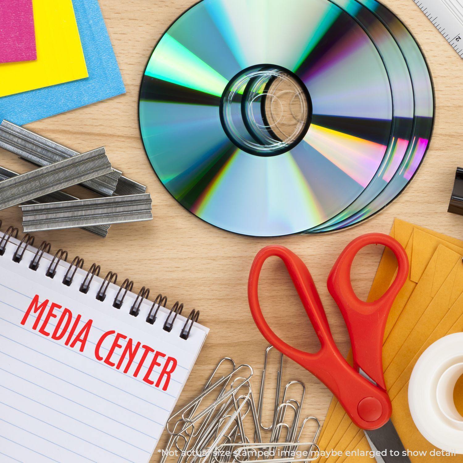 Desk with CDs, paper clips, red scissors, staples, and a notepad stamped with MEDIA CENTER using the Large Media Center Rubber Stamp.