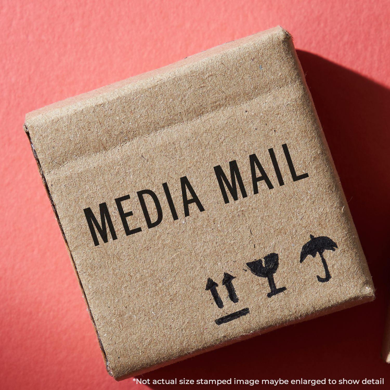 A cardboard box stamped with MEDIA MAIL using a Slim Pre-Inked Media Mail Stamp, placed on a red background.