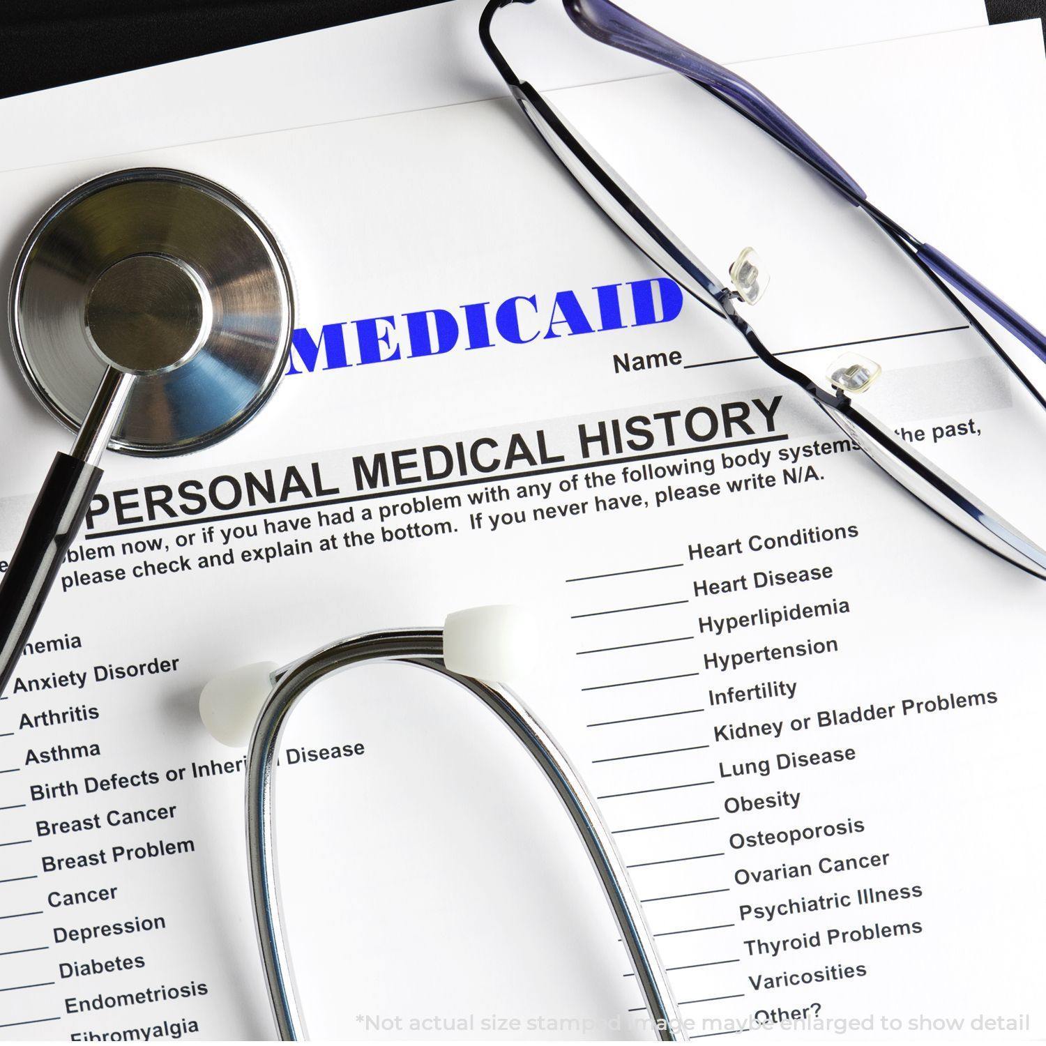 A Large Self Inking Medicaid Stamp is shown on a medical history form with a stethoscope and glasses nearby.