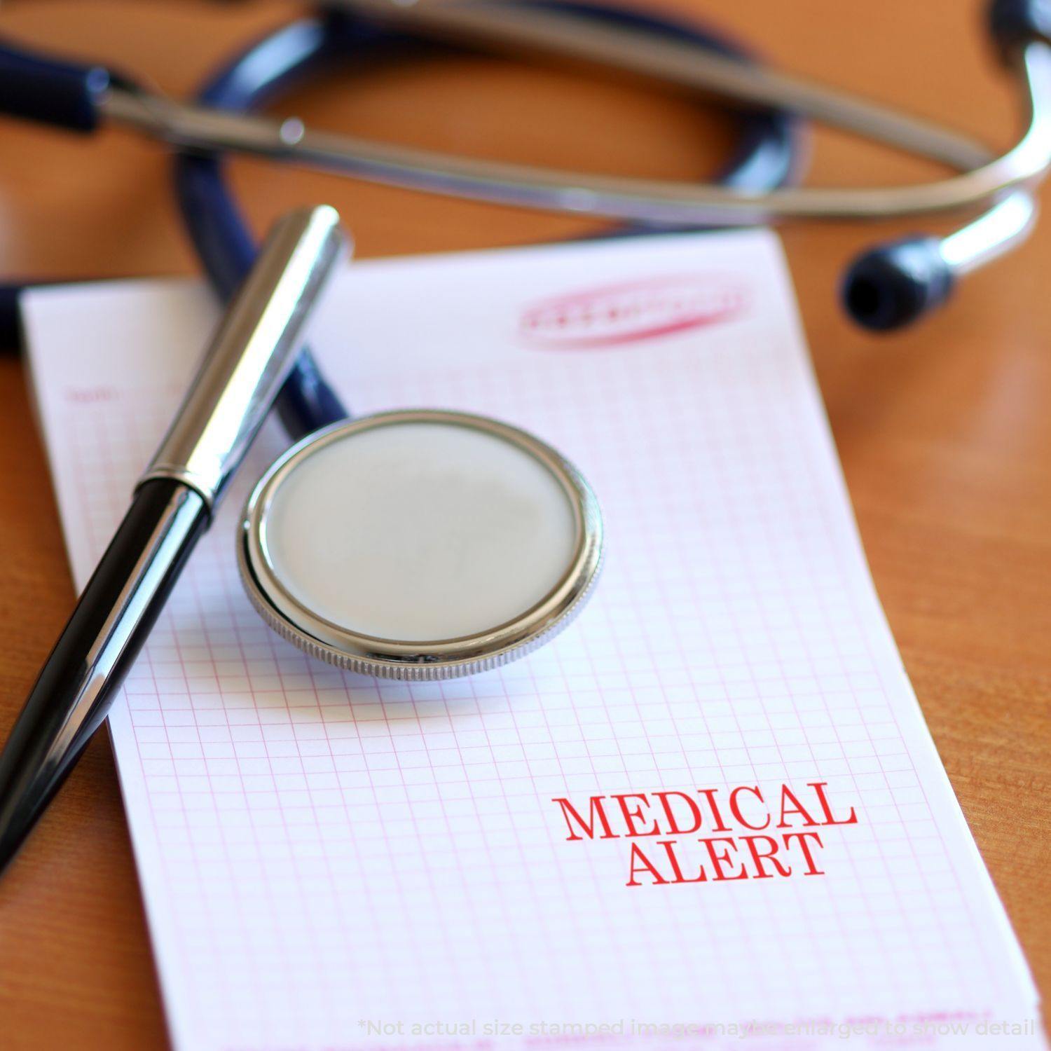 Slim Pre-Inked Medical Alert Stamp on a notepad with MEDICAL ALERT text, next to a stethoscope and pen on a wooden desk.