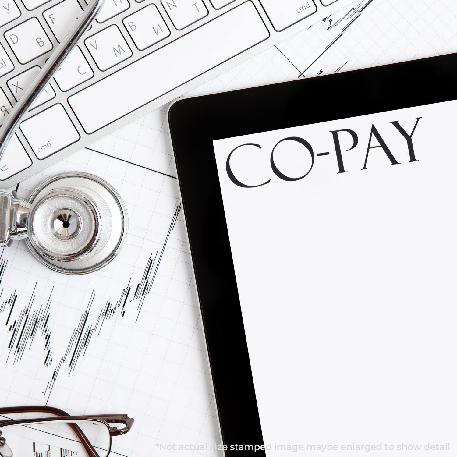 Large Co Pay Rubber Stamp used on a document near a stethoscope, keyboard, and tablet displaying the word CO-PAY .