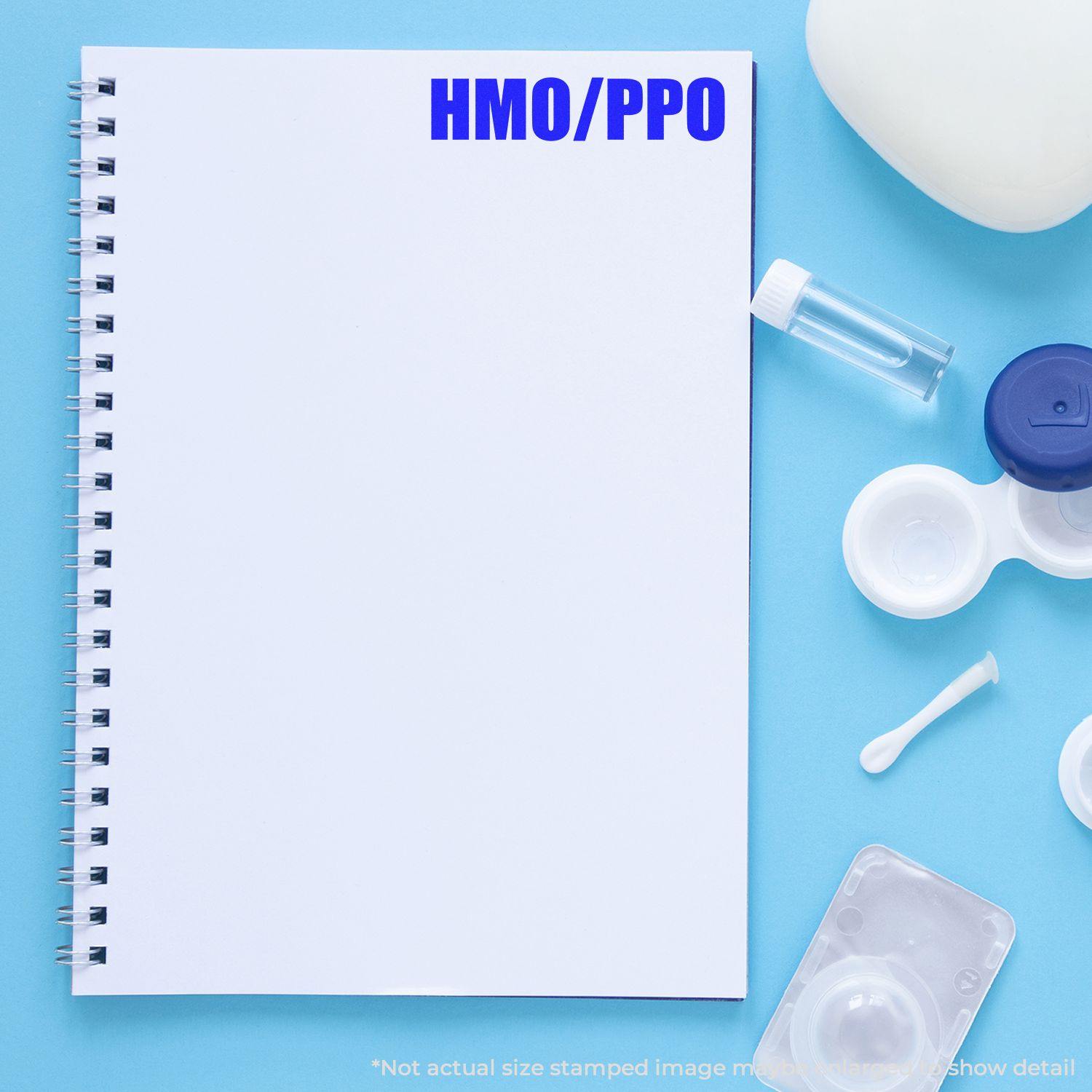 Large Pre-Inked HMO/PPO Stamp used on a blank spiral notebook, surrounded by medical items on a blue background.