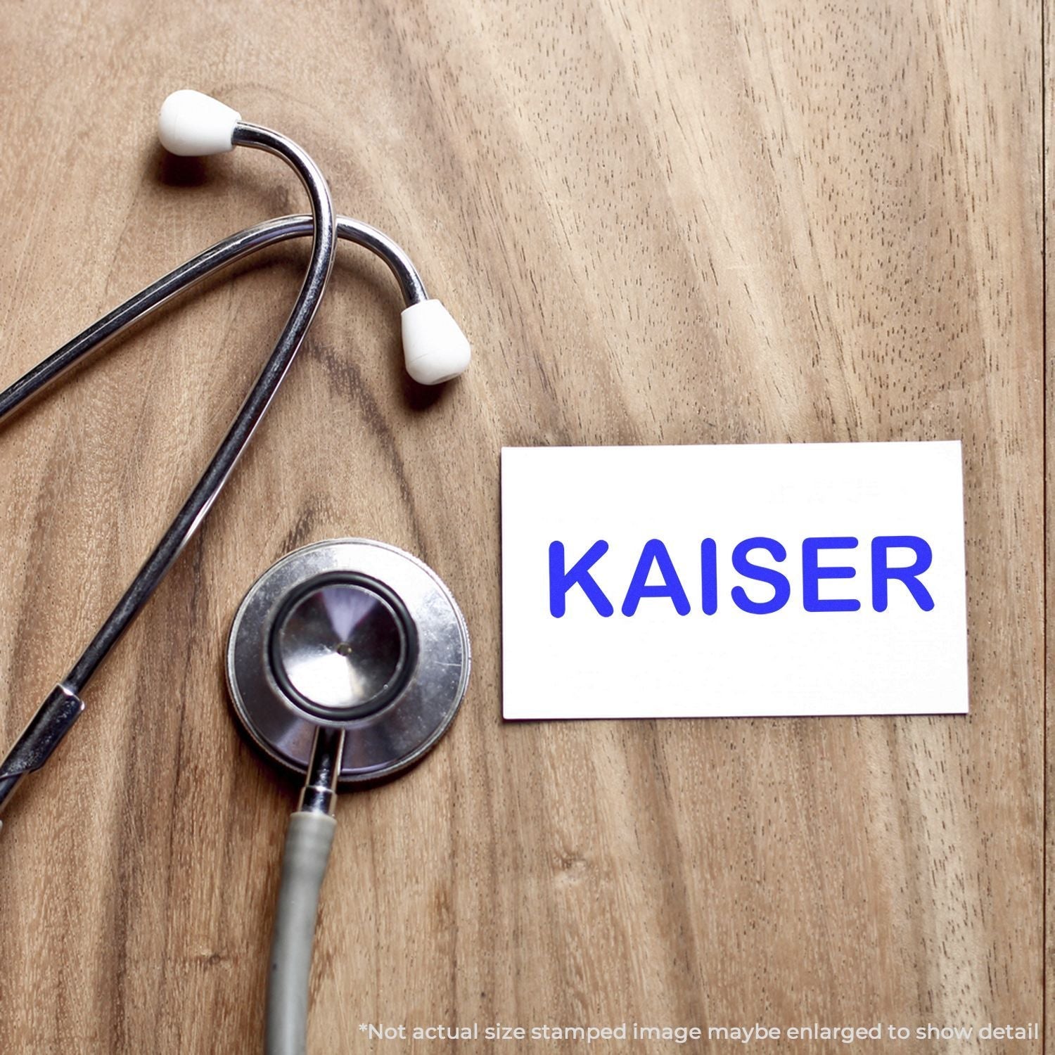 Self Inking Kaiser Stamp on a wooden surface next to a stethoscope, with the word KAISER stamped in blue on a white card.