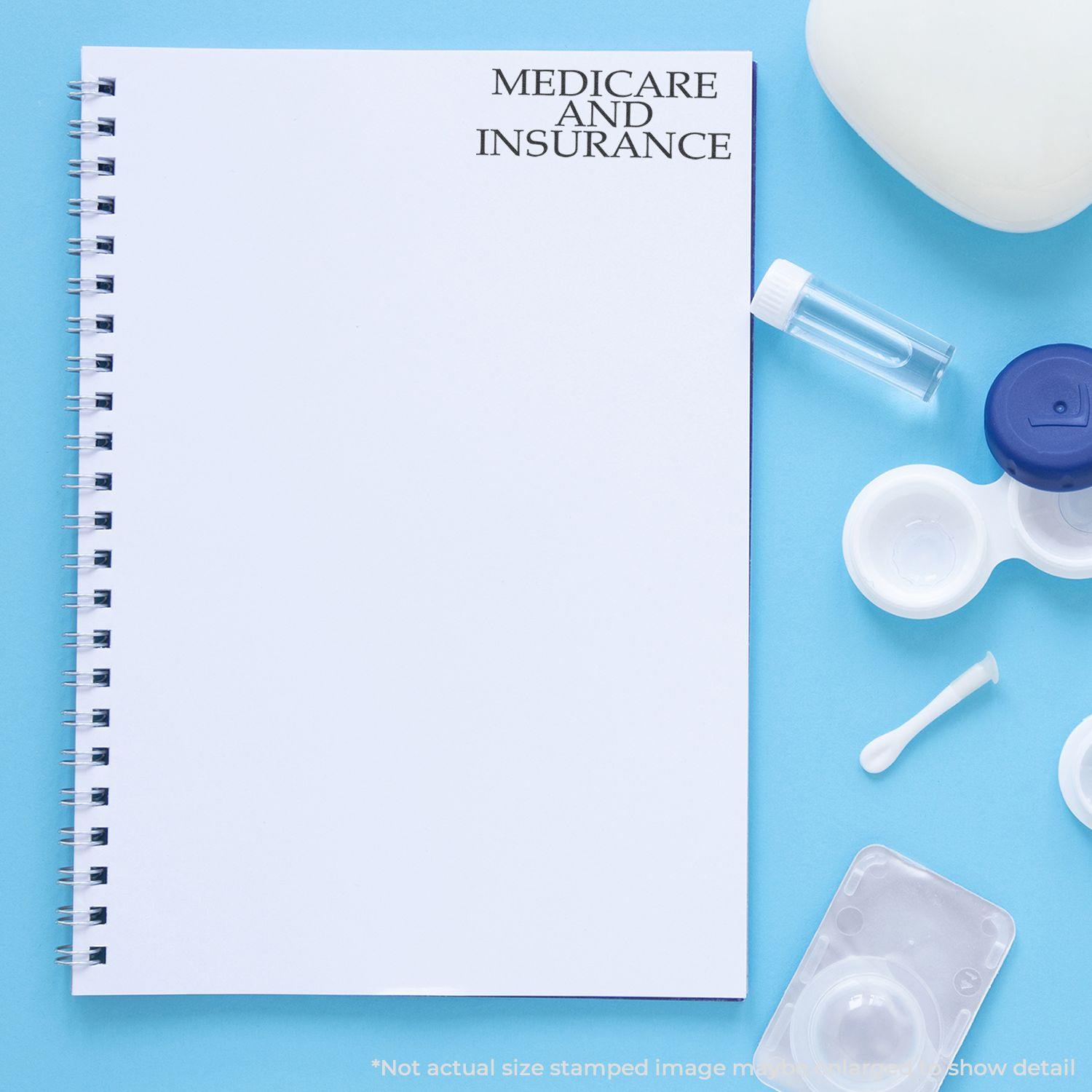 Large Medicare And Insurance Rubber Stamp used on a blank spiral notebook, surrounded by medical items on a blue background.