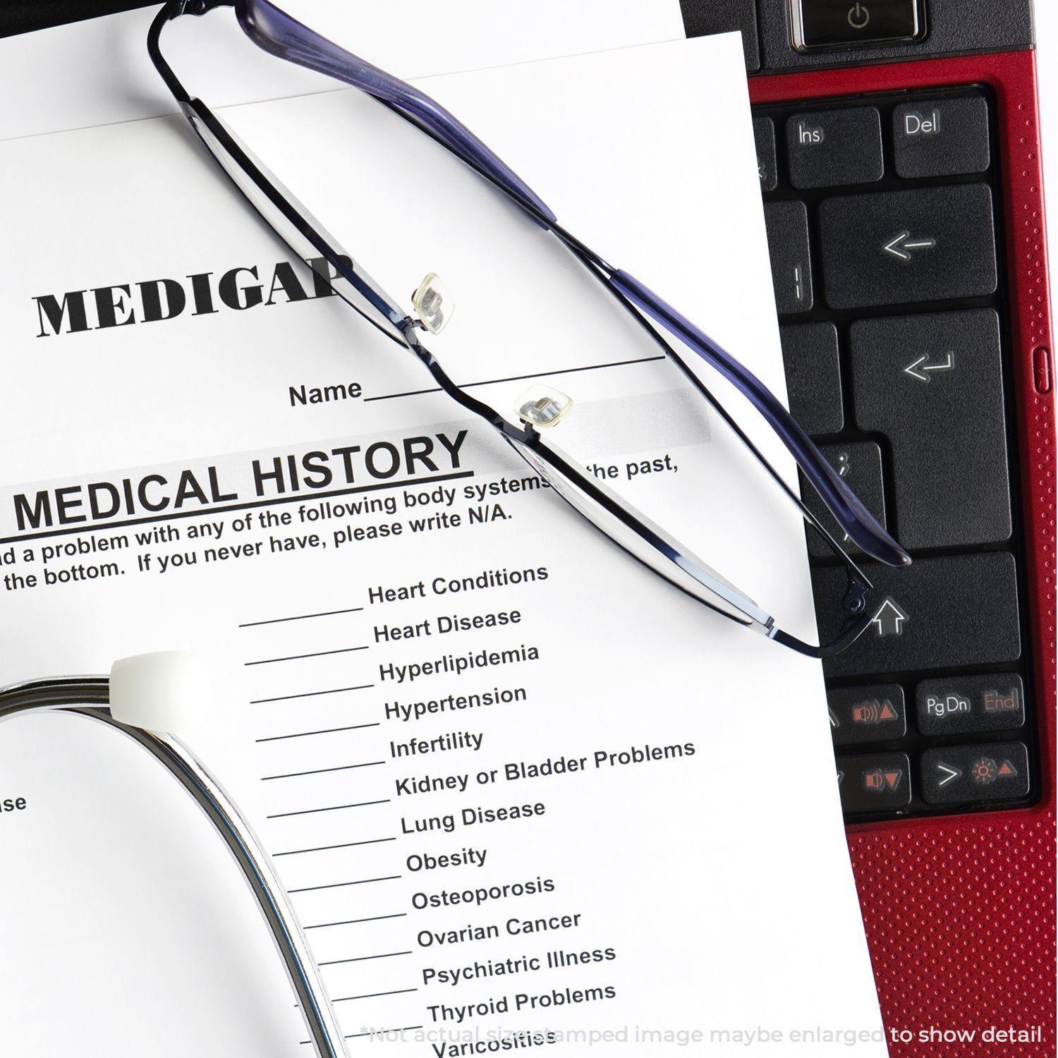 Slim Pre-Inked Medigap Stamp on a medical history form with glasses and a stethoscope on a laptop keyboard.