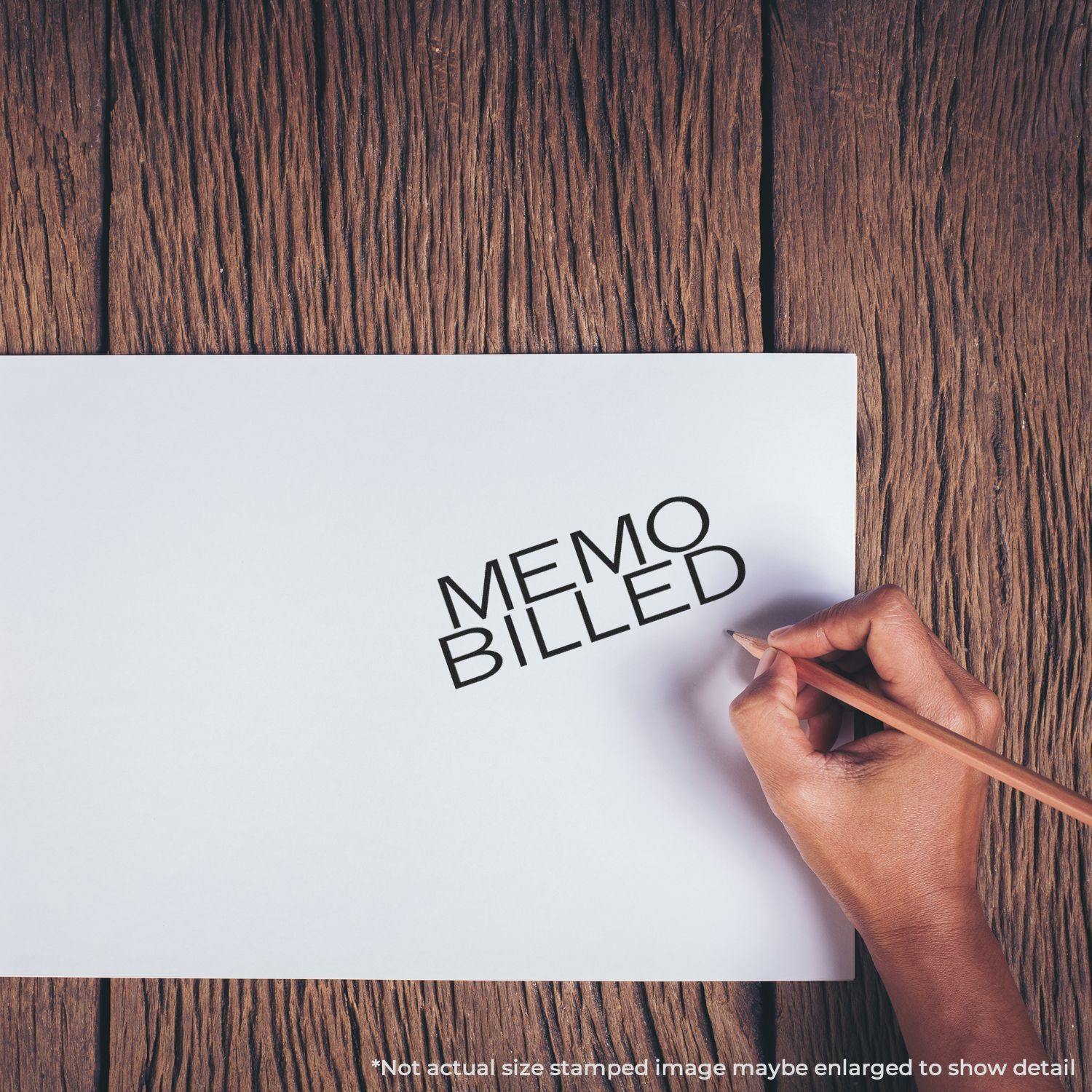 Hand using Large Pre-Inked Memo Billed Stamp on white paper, wooden surface background. Text MEMO BILLED stamped in black.