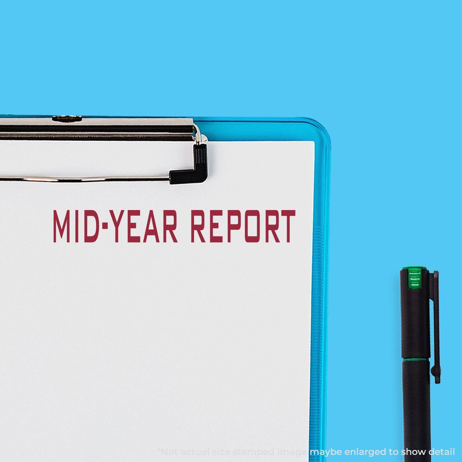 Clipboard with a stamped MID-YEAR REPORT in red ink, using the Large Mid Year Report Rubber Stamp, next to a black pen on a blue background.