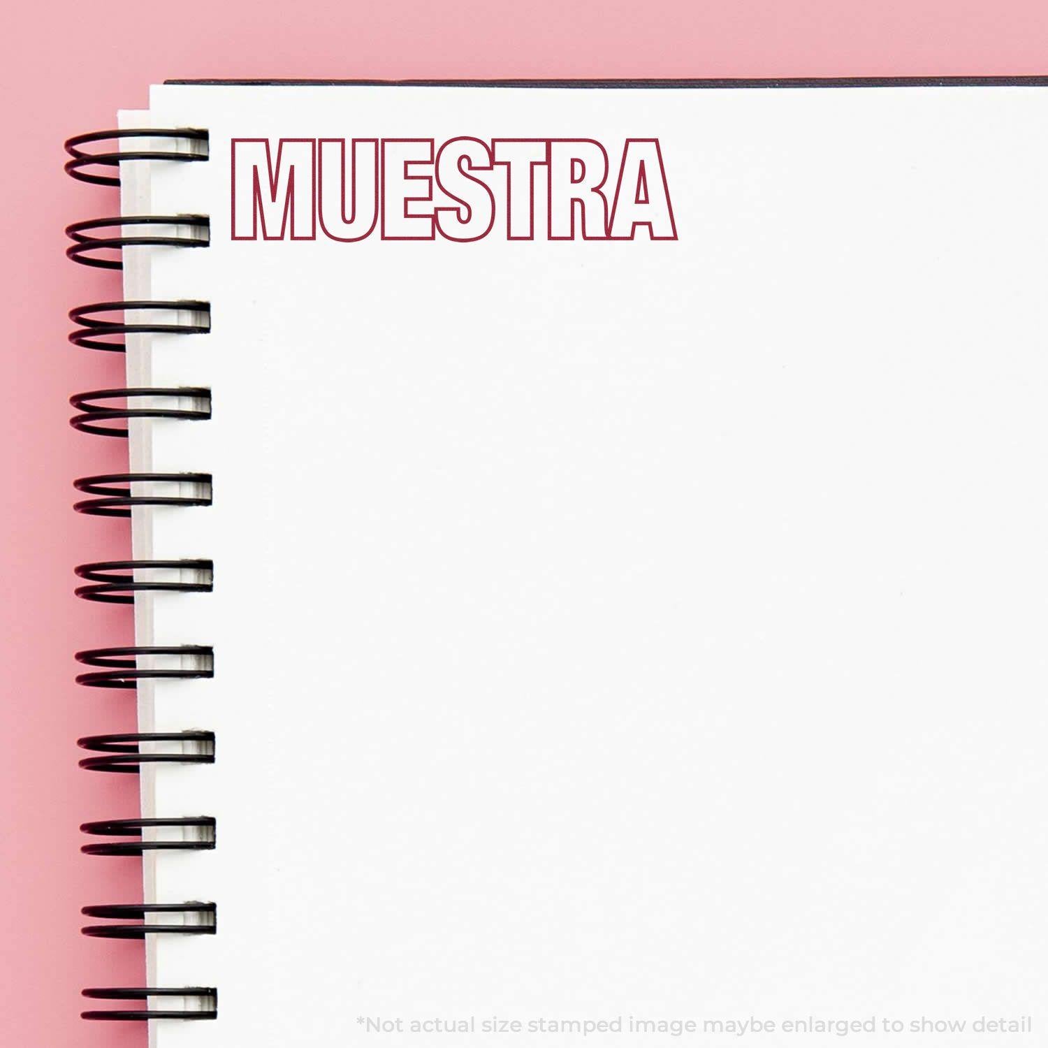 Large Pre-Inked Muestra Stamp in red ink on a white spiral notebook with a pink background.