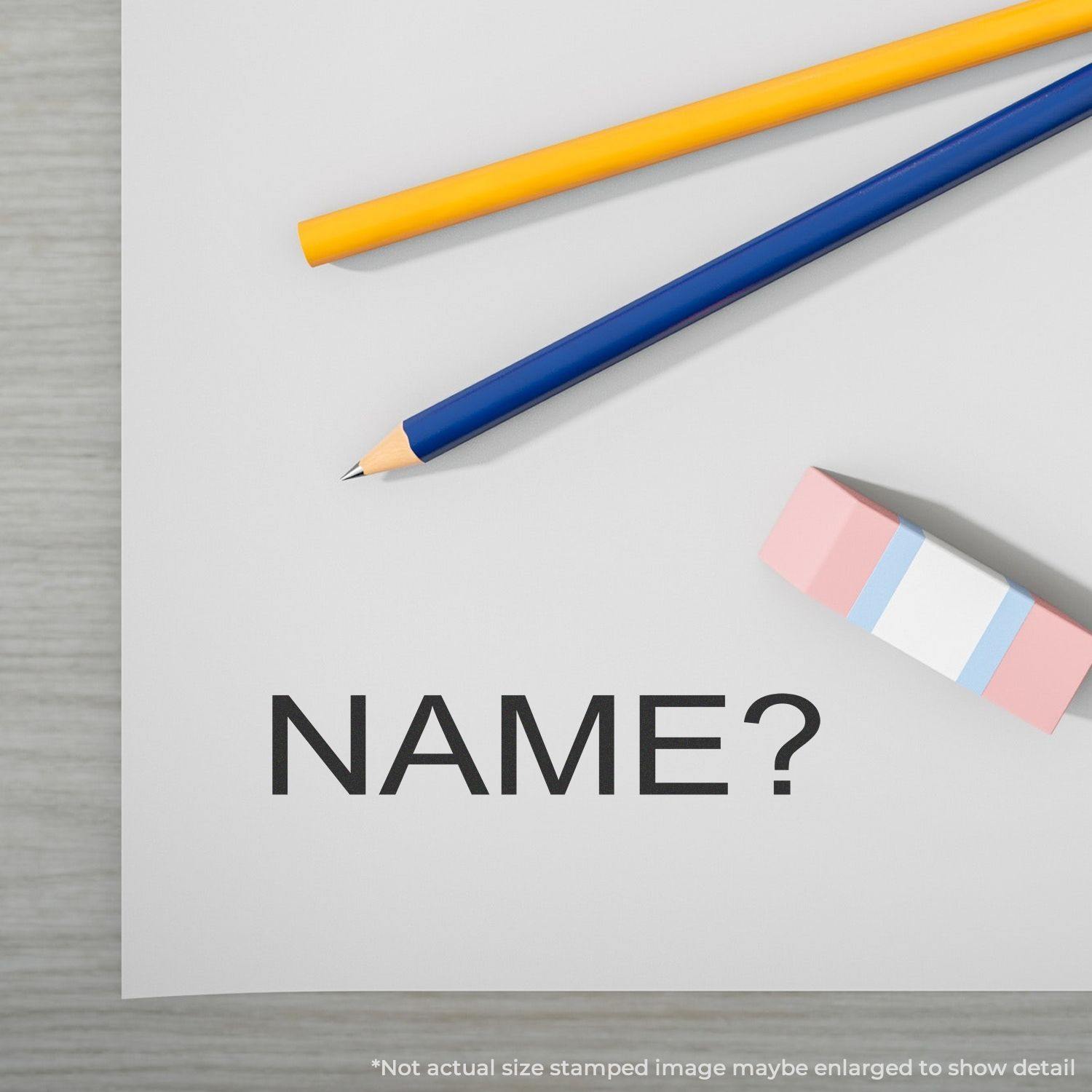 Slim Pre-Inked Name Stamp on a white paper with NAME? text, alongside a yellow pencil, blue pencil, and pink eraser.