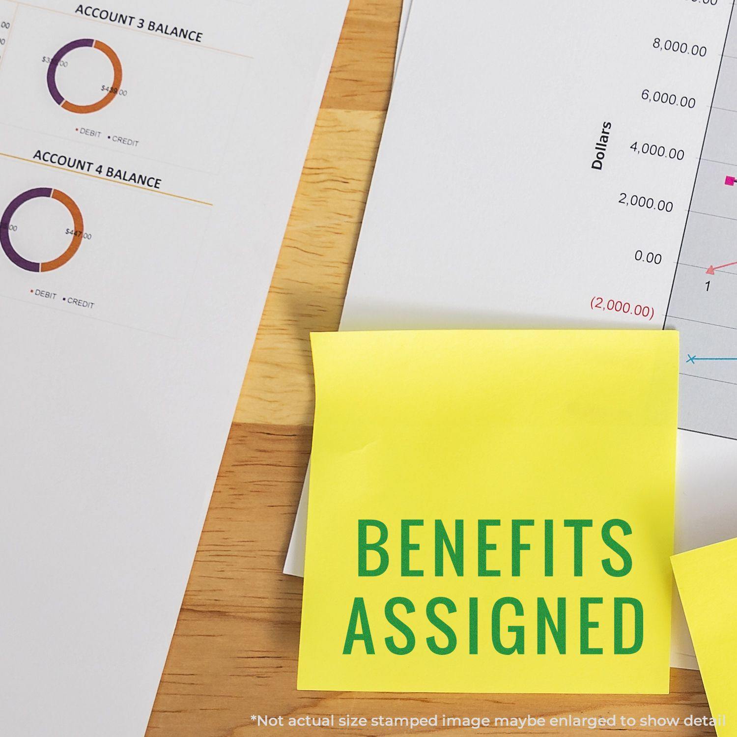 A Large Narrow Benefits Assigned Rubber Stamp is used on a yellow sticky note, placed on a desk with financial documents.