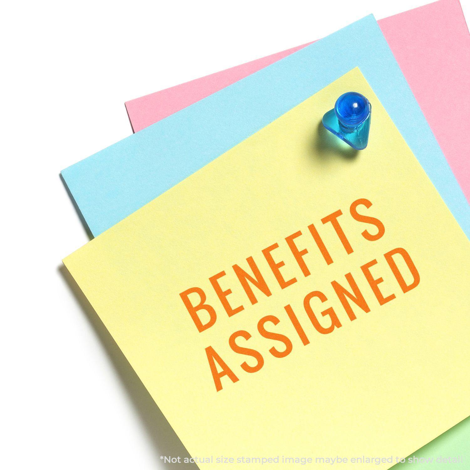 Large Self Inking Narrow Benefits Assigned Stamp marking BENEFITS ASSIGNED on a yellow paper pinned to a board with blue and pink papers.