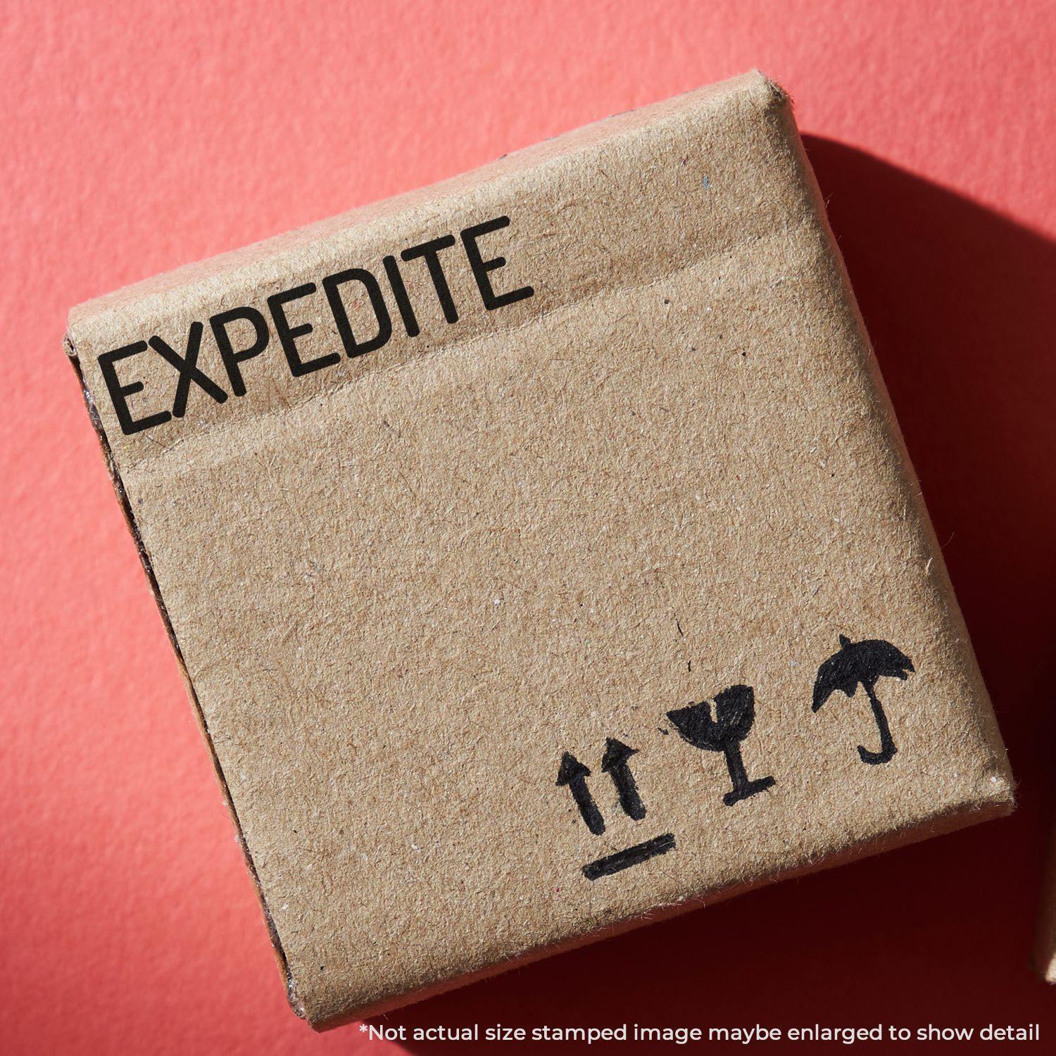 A cardboard box stamped with EXPEDITE using the Large Narrow Expedite Rubber Stamp, placed on a red background.