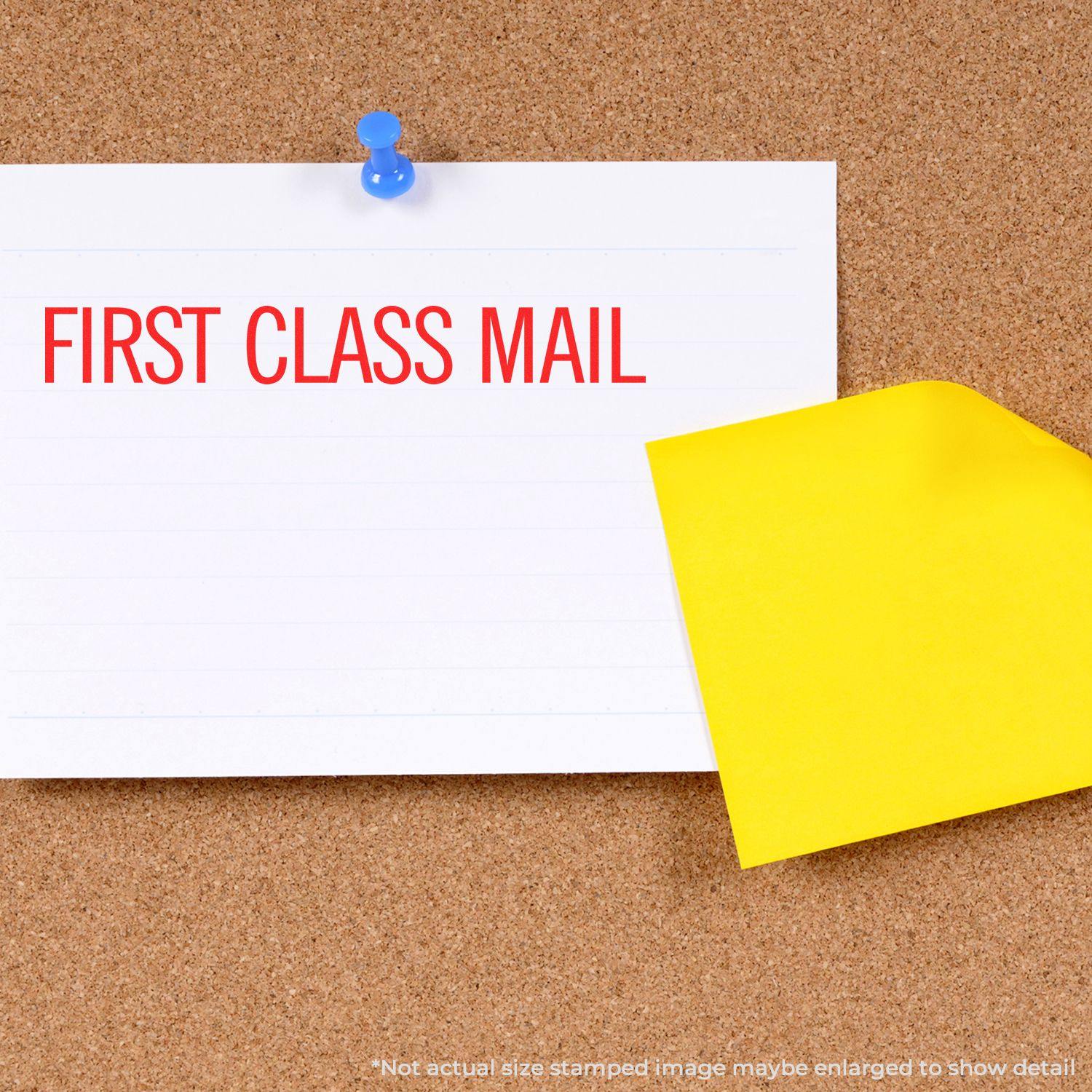 A Large Pre-Inked Narrow First Class Mail Stamp imprint on a white card pinned to a corkboard with a yellow sticky note partially covering it.