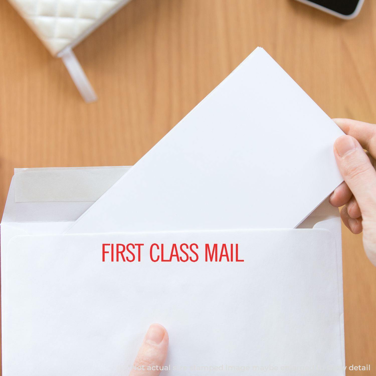 Person holding an envelope stamped with FIRST CLASS MAIL using the Large Self Inking Narrow First Class Mail Stamp on a wooden table.