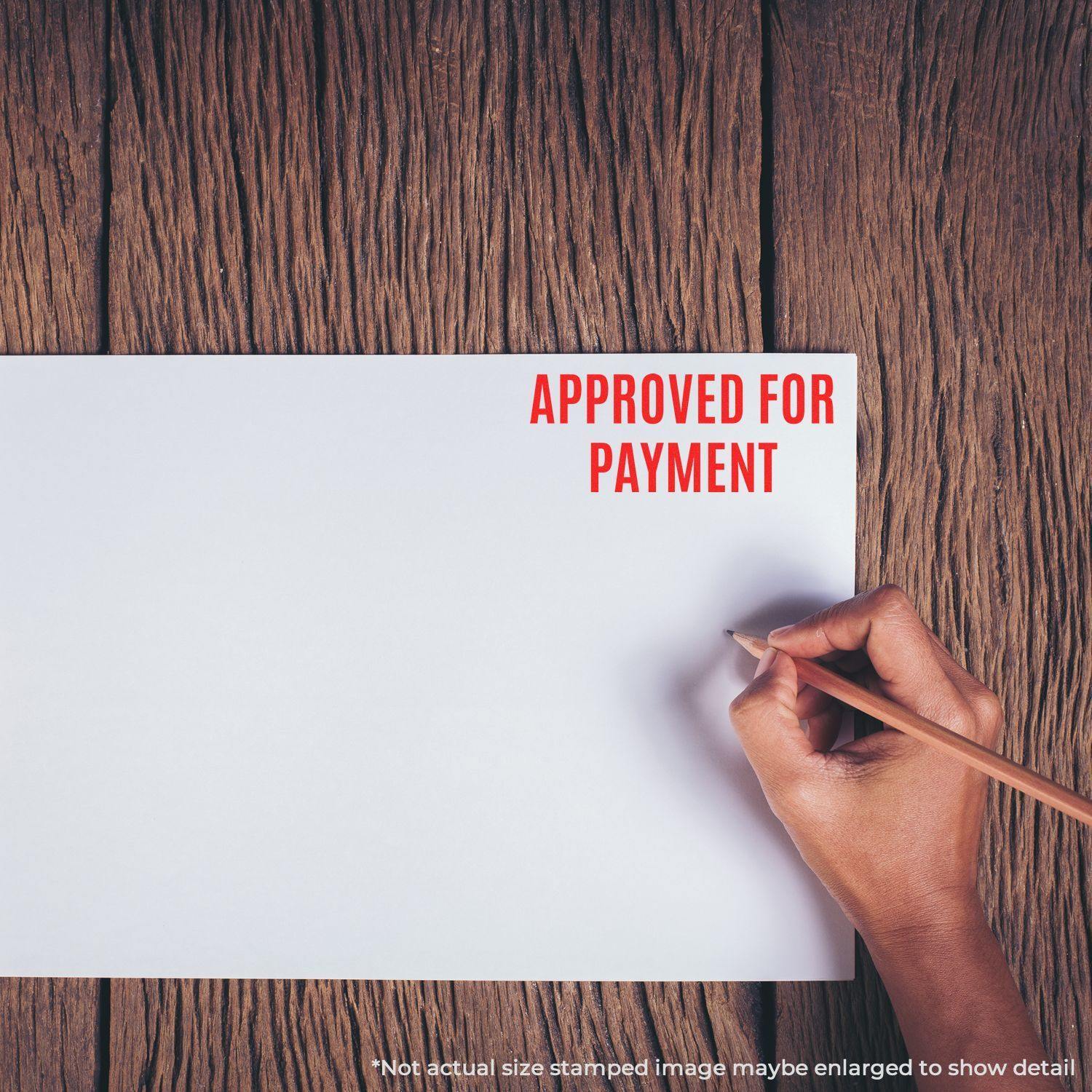 A hand holding a pencil next to a paper stamped with APPROVED FOR PAYMENT using the Large Narrow Font Approved for Payment Rubber Stamp.