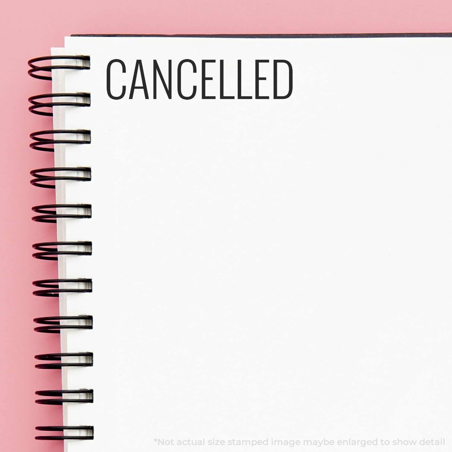 Large Pre-Inked Narrow Font Cancelled Stamp used on a white spiral notebook, displaying the word CANCELLED in black ink on a pink background.