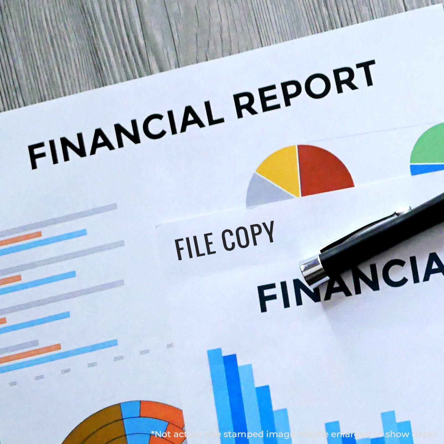 Financial reports stamped with FILE COPY using the Large Narrow Font File Copy Rubber Stamp, with charts and a pen on a wooden desk.