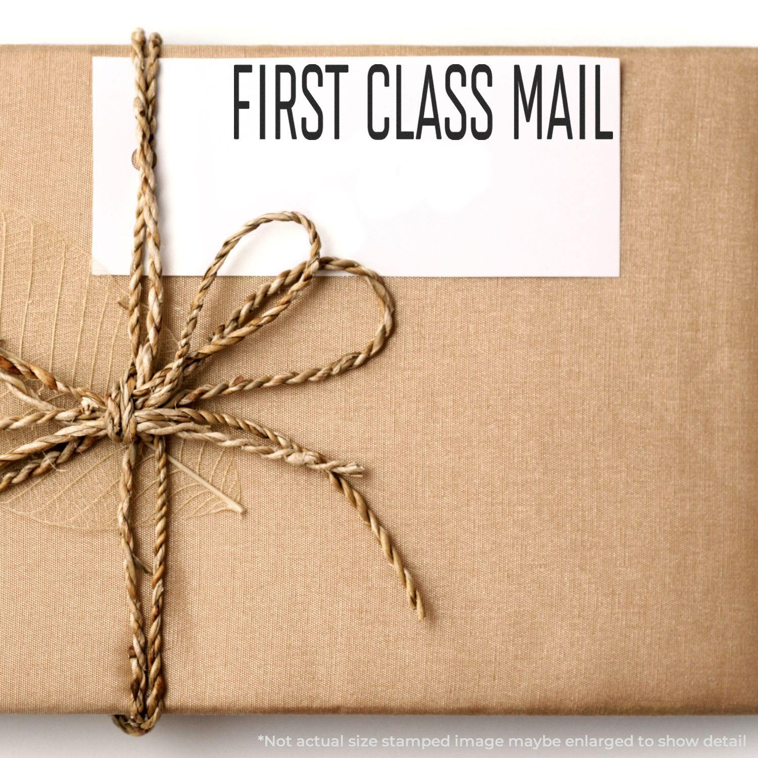 A package wrapped in brown paper with a twine bow and a Large Narrow Font First Class Mail Rubber Stamp imprint on a white label.