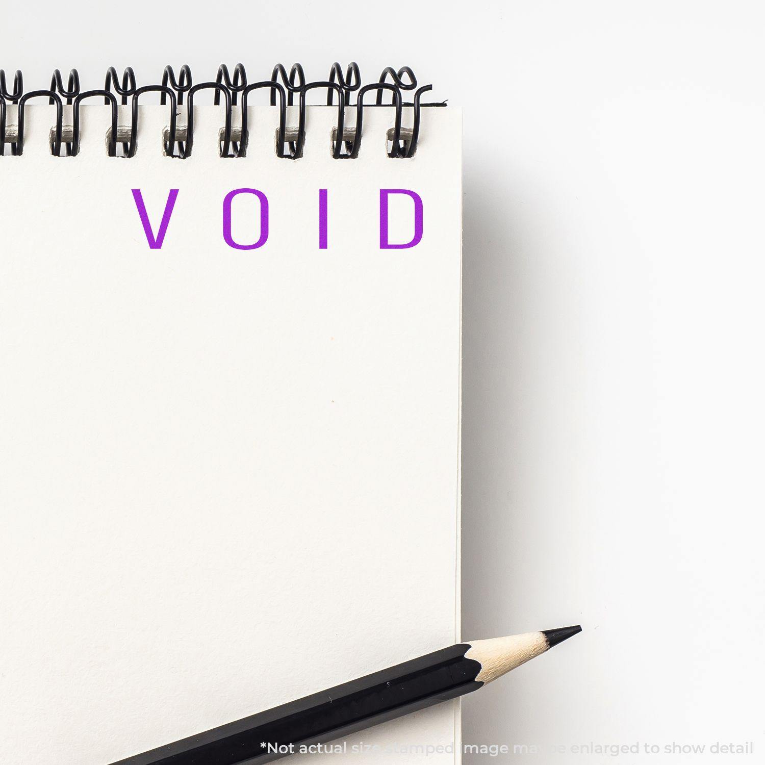 Narrow Void Rubber Stamp imprint on a white notepad with a pencil beside it. The word VOID is stamped in purple ink.