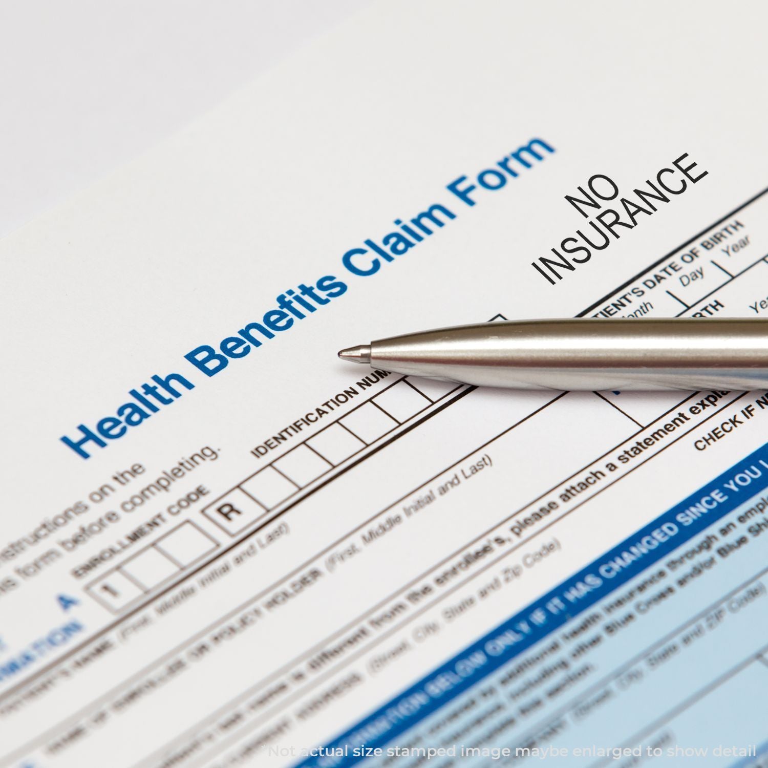 A Health Benefits Claim Form stamped with NO INSURANCE using a Self Inking No Insurance Stamp, with a pen placed on the form.