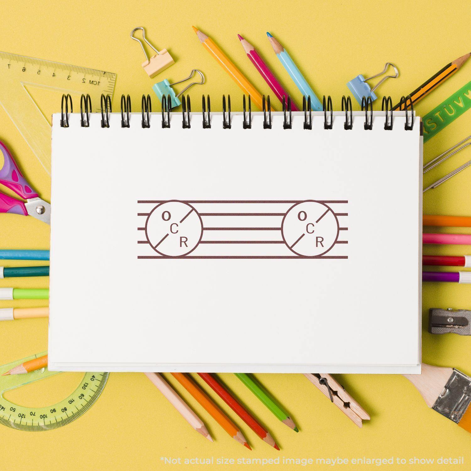 A Large Self Inking OCR Stamp imprint on a white notebook page surrounded by colorful stationery on a yellow background.