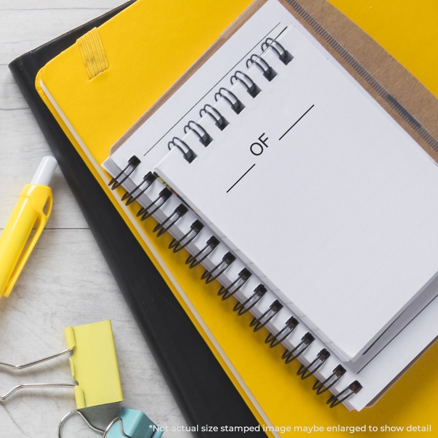 Self Inking Pkg Of Stamp in use on a spiral notebook, placed on top of yellow and black folders with a pen and binder clips nearby.