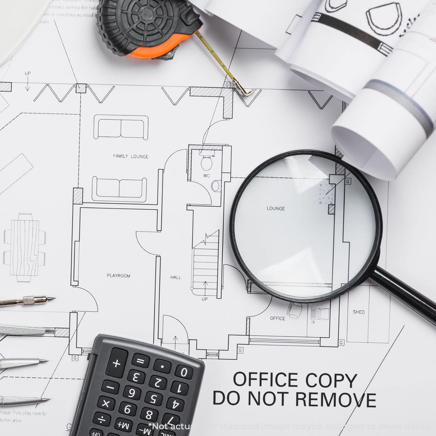 A Large Office Copy Do Not Remove Rubber Stamp is placed on architectural blueprints with a magnifying glass, calculator, and measuring tape.