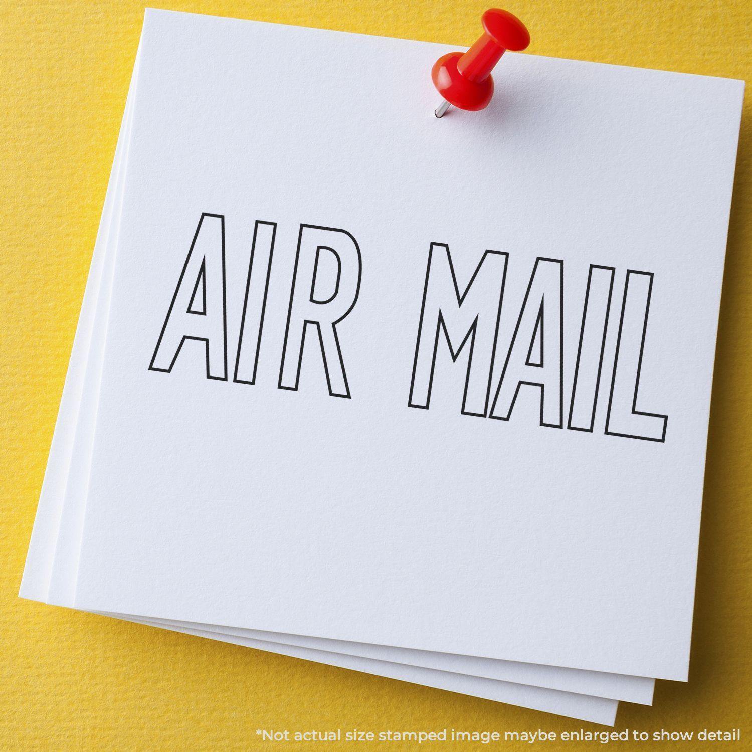 A white card with AIR MAIL stamped using the Large Outline Air Mail Rubber Stamp, pinned to a yellow surface with a red pushpin.