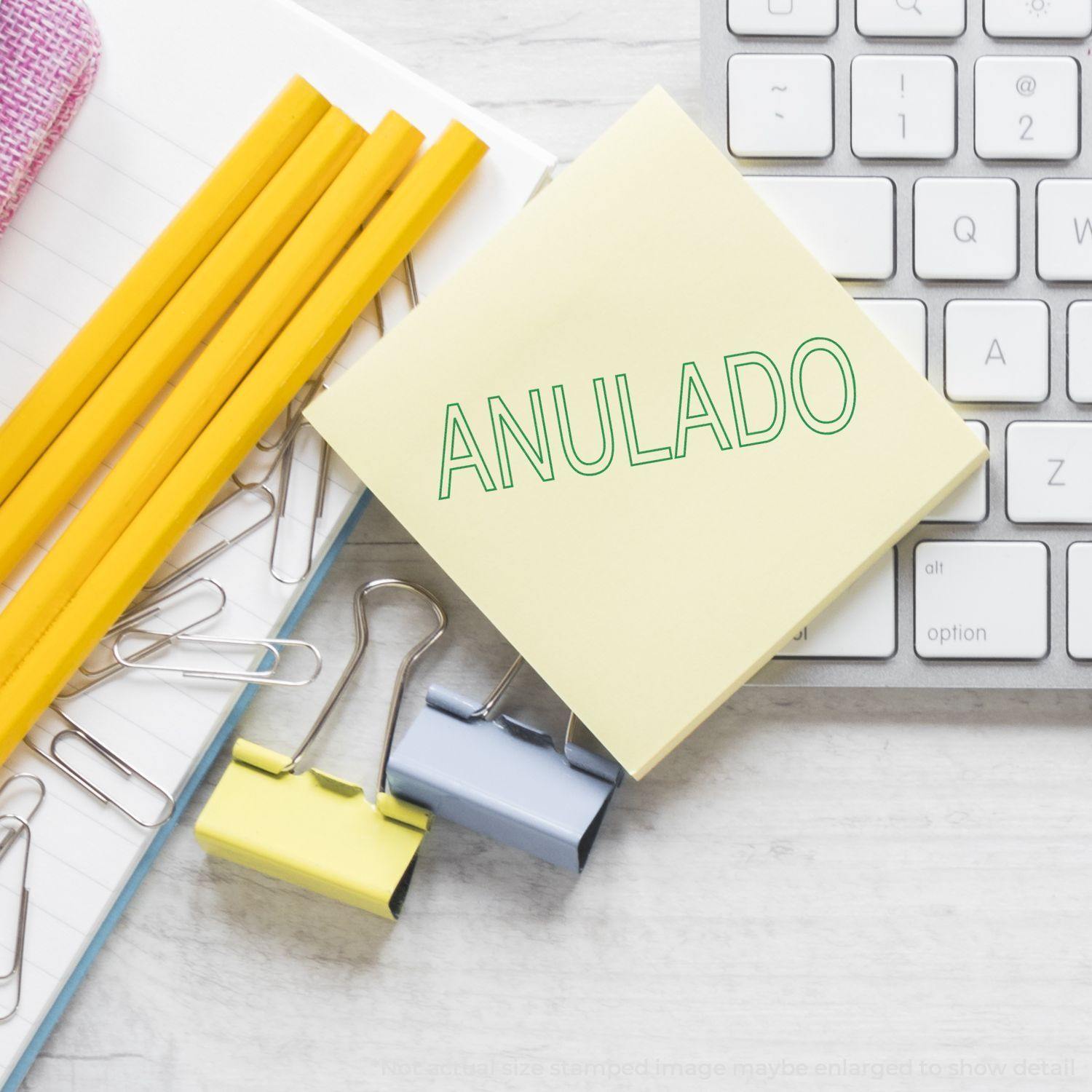 Large Pre-Inked Outline Anulado Stamp on a yellow sticky note, surrounded by pencils, paper clips, binder clips, and a keyboard.