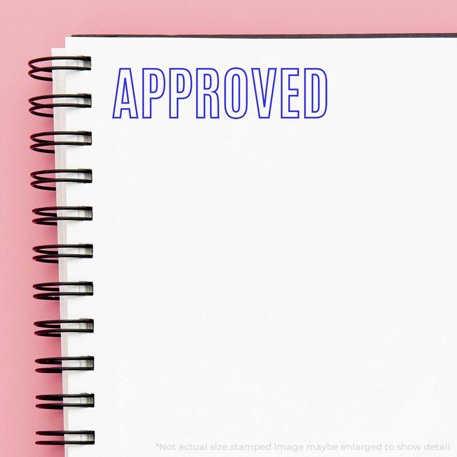 Large Pre-Inked Outline Approved Stamp used on a white spiral notebook, displaying the word APPROVED in blue ink on a pink background.