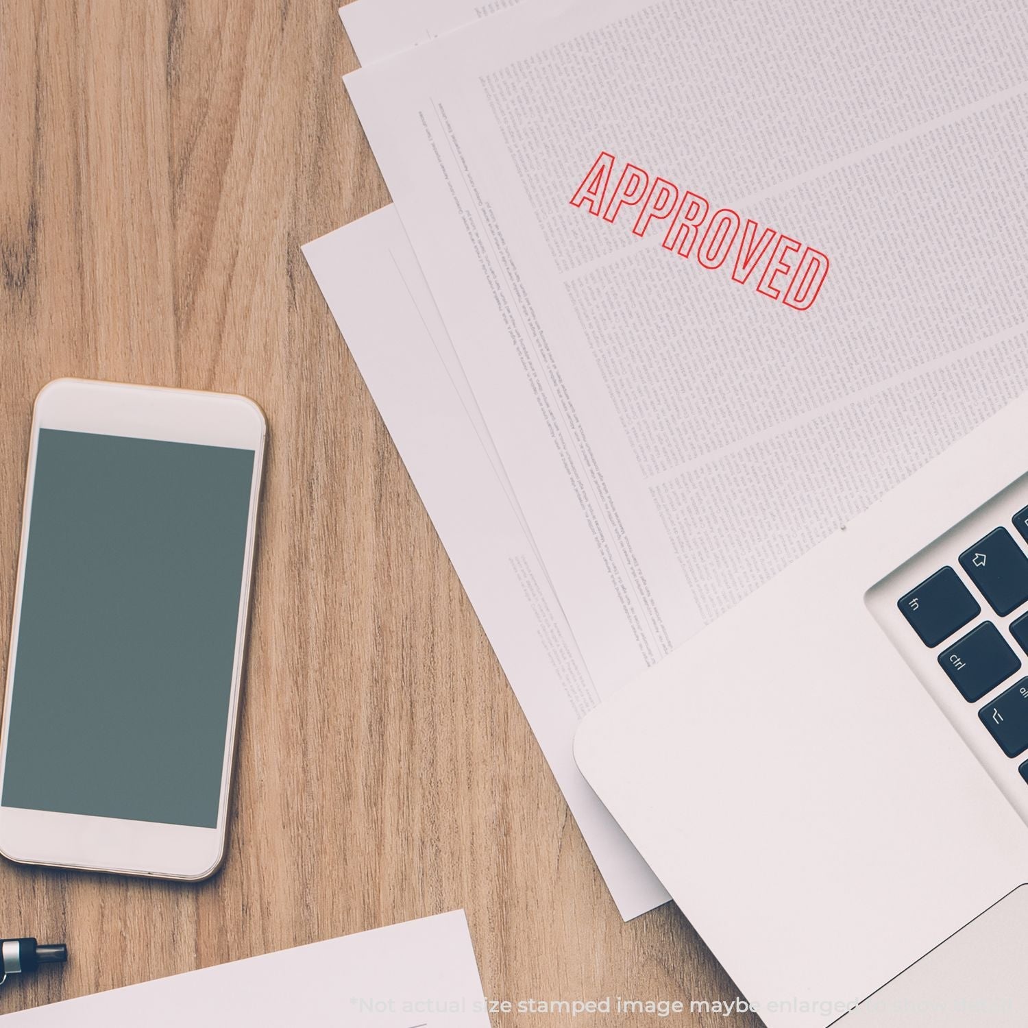 Self Inking Outline Approved Stamp used on a document next to a smartphone and laptop on a wooden desk.