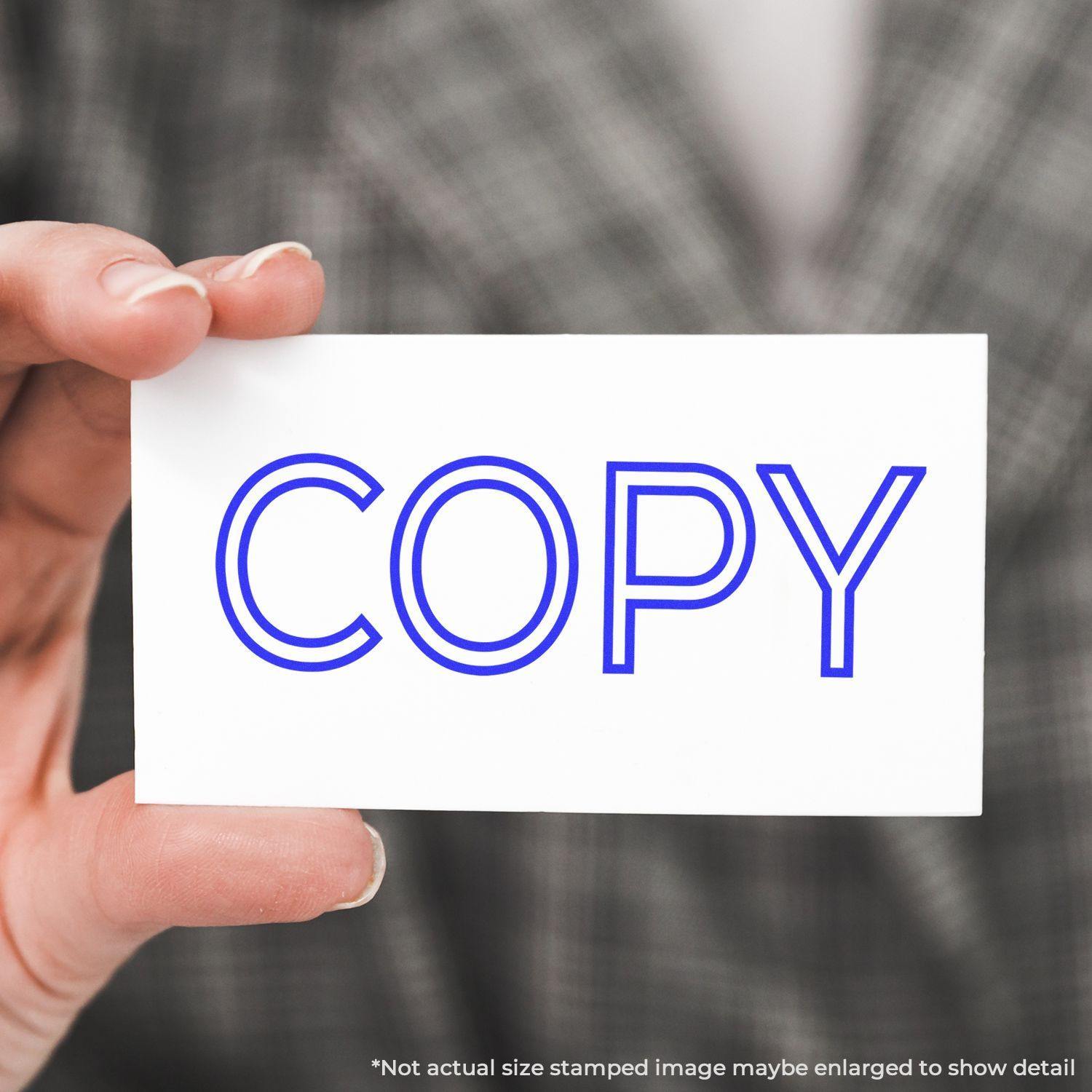 A hand holding a card stamped with the word COPY in blue using the Large Outline Copy Rubber Stamp.