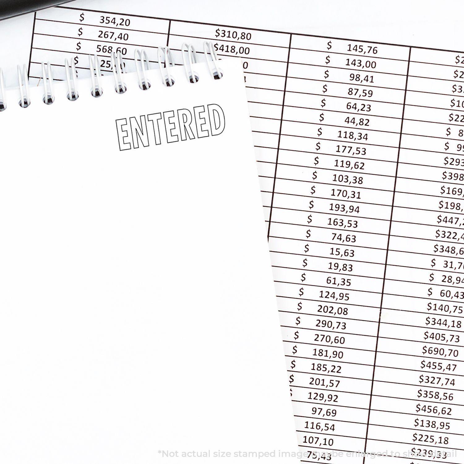 Notebook with ENTERED stamped using the Large Entered With Outline Rubber Stamp, placed next to a financial spreadsheet.