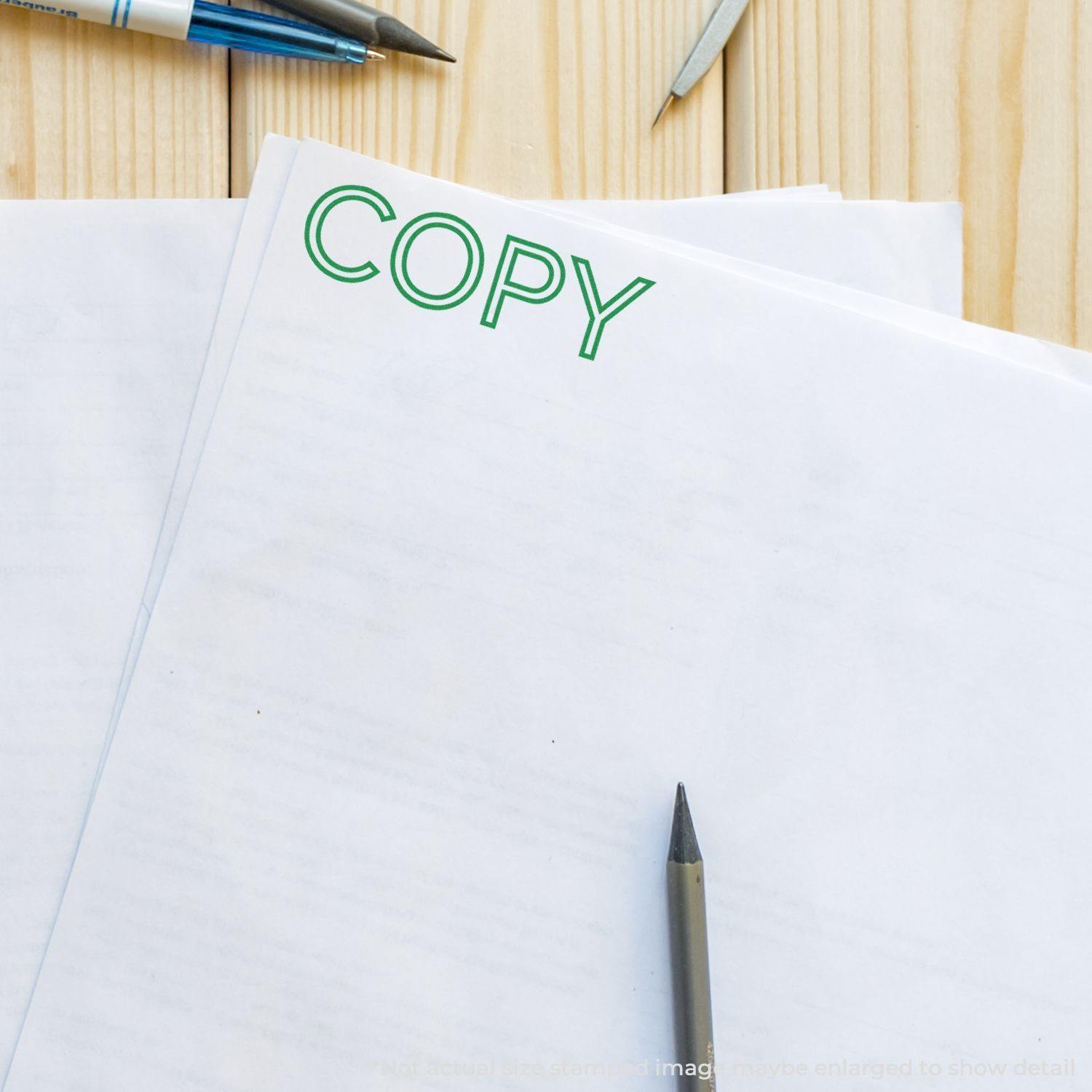 Outline Font Copy Rubber Stamp used on a stack of papers, with pens and a wooden surface in the background.