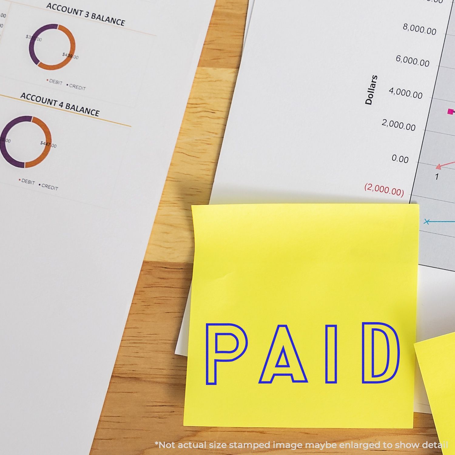 Self Inking Outline Paid Stamp marking PAID on a yellow sticky note, placed on financial documents with charts and graphs.