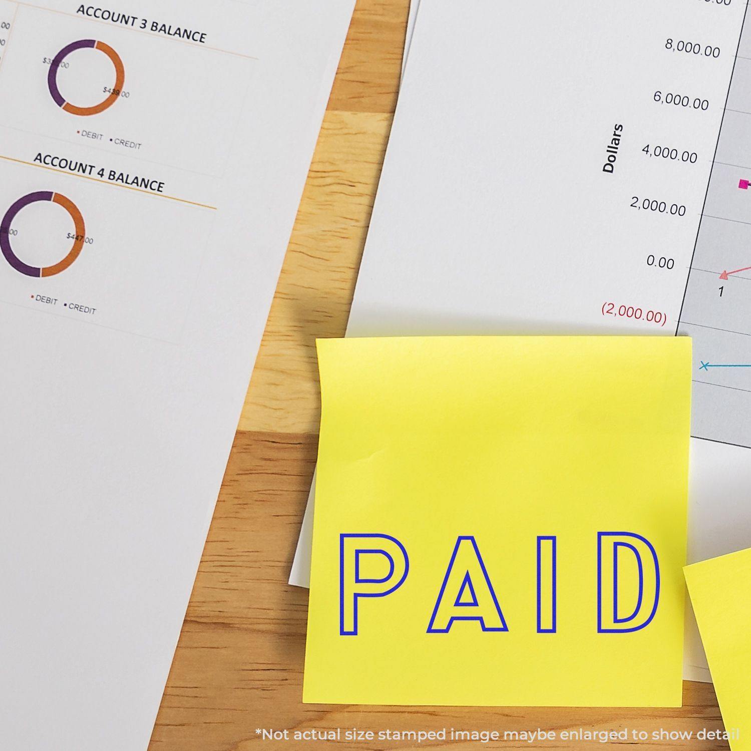 Large Pre-Inked Outline Paid Stamp used on a yellow sticky note, placed on financial documents with charts and graphs on a wooden desk.