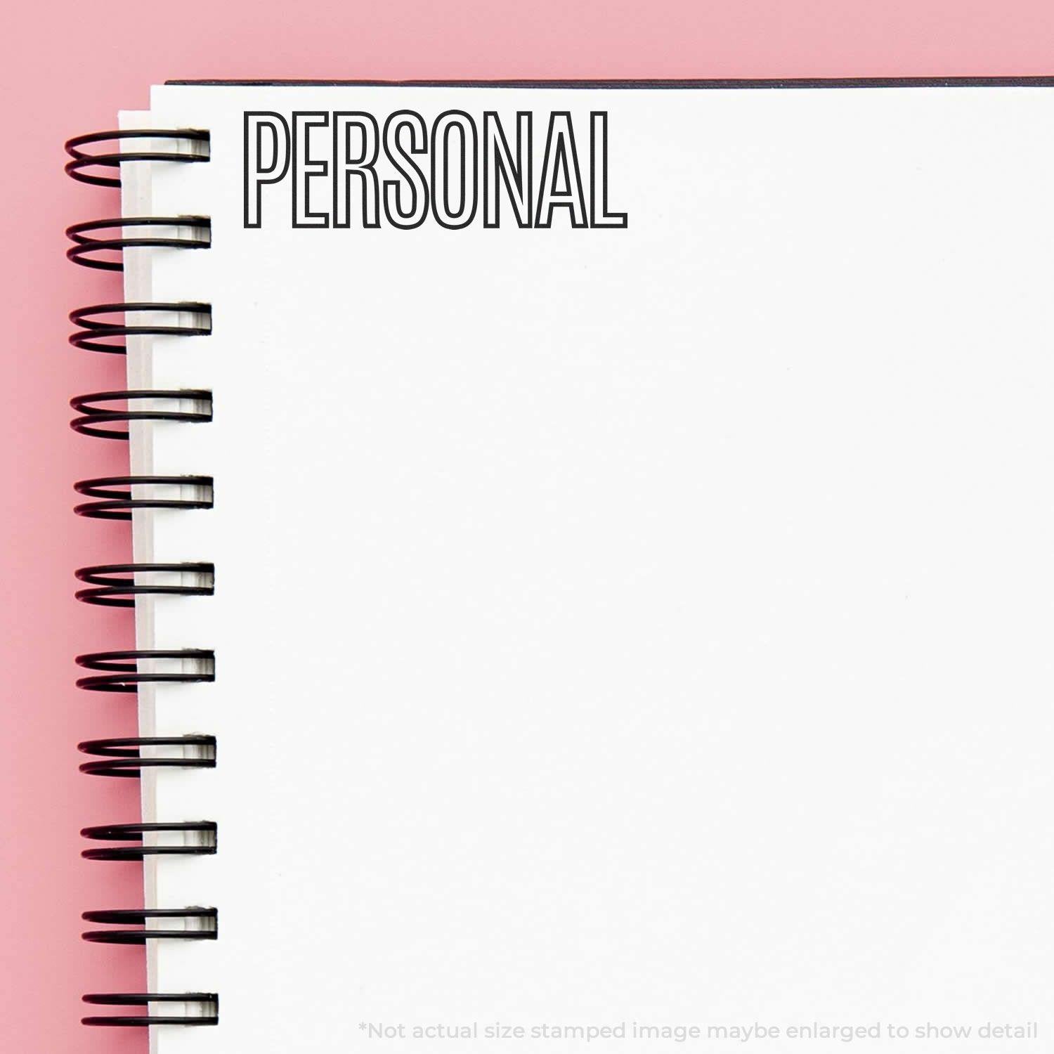 A notebook with a spiral binding and the word PERSONAL stamped on it using the Large Outline Personal Rubber Stamp against a pink background.