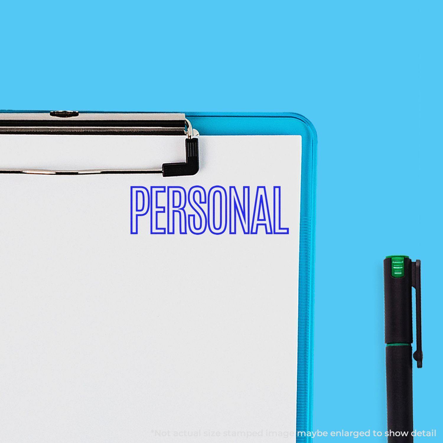 Large Pre-Inked Outline Personal Stamp in blue ink on white paper, next to a black pen with a green clip, on a blue background.