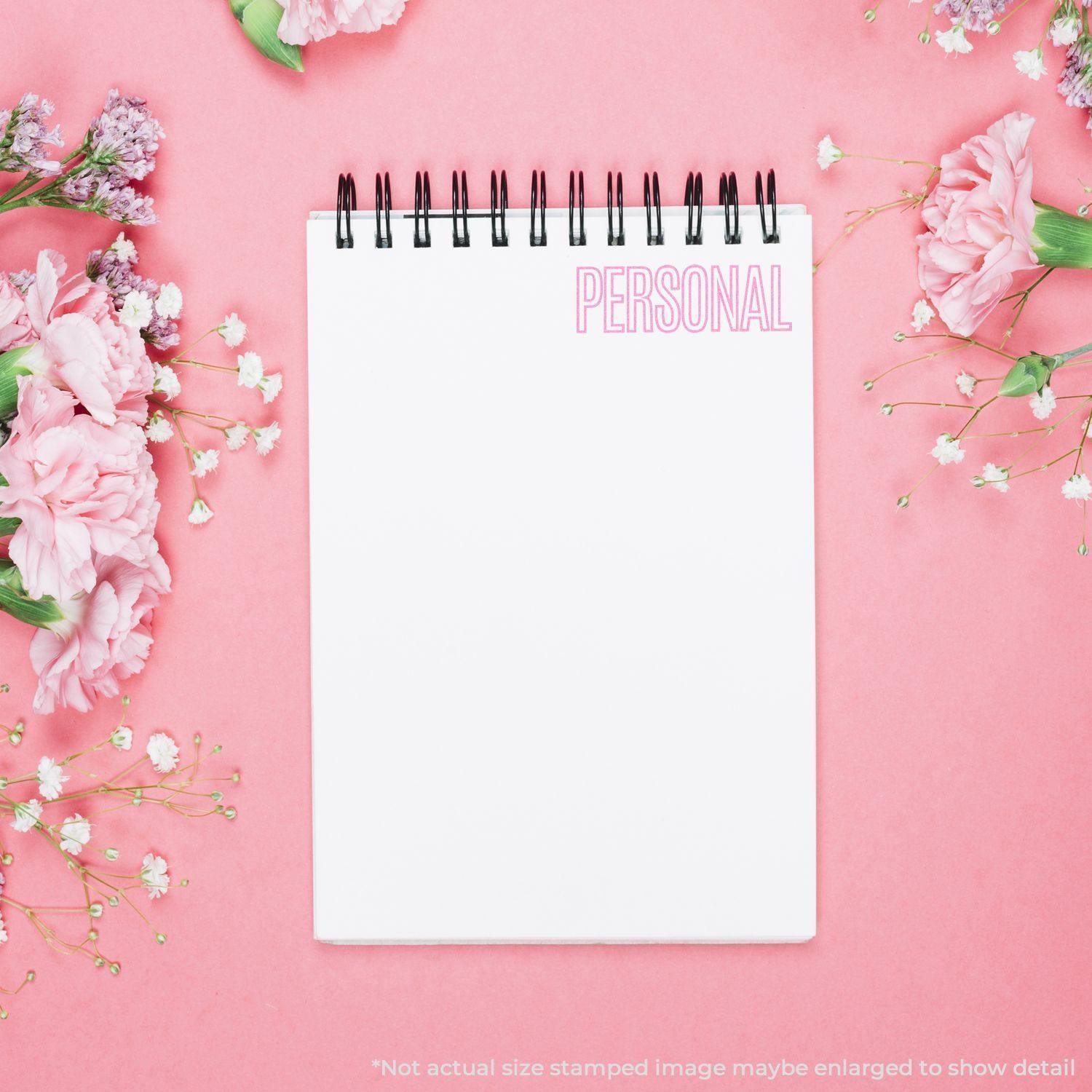 Large Pre-Inked Outline Personal Stamp in pink ink on a white notepad, surrounded by pink flowers on a pink background.