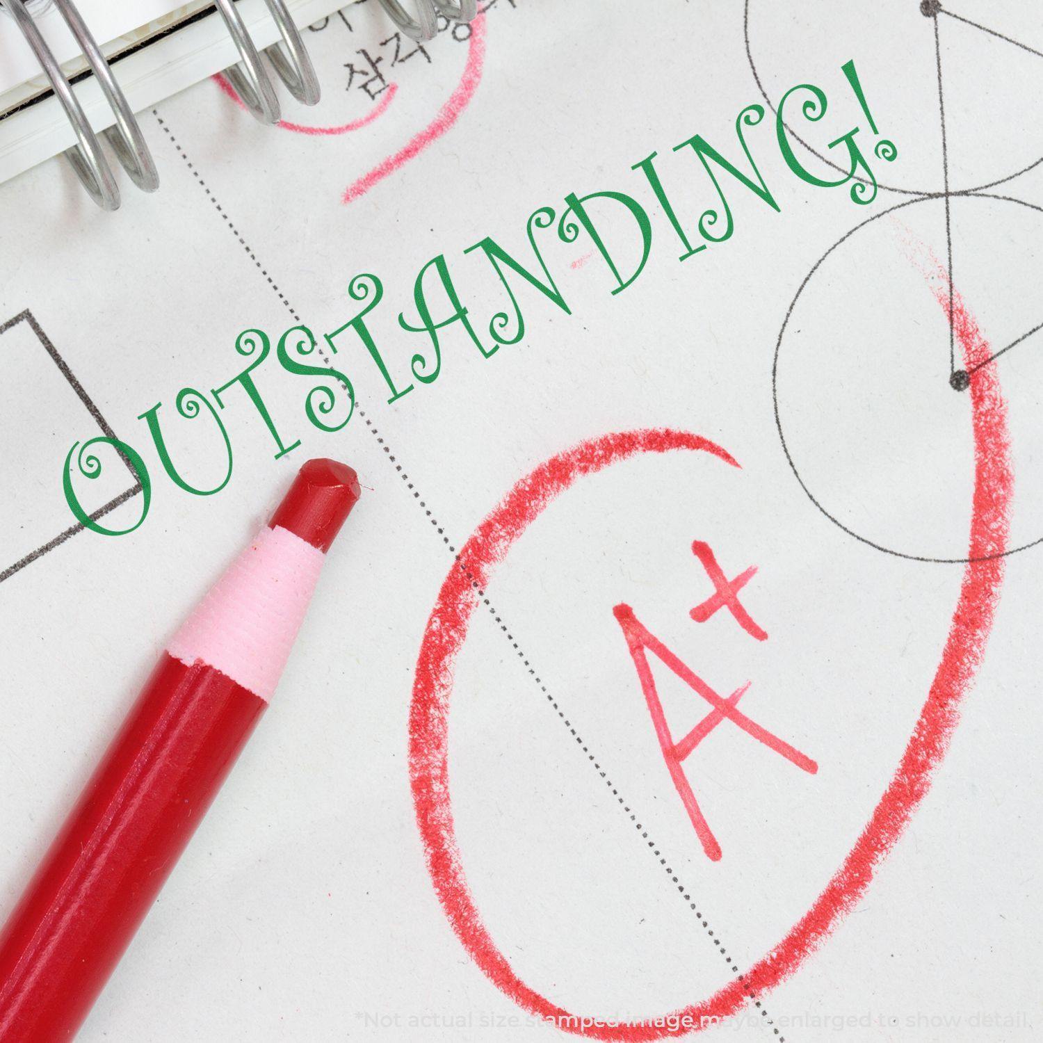 A red pen marks an A+ on a paper with a green "OUTSTANDING!" stamped using the Large Pre-Inked Outstanding Stamp.