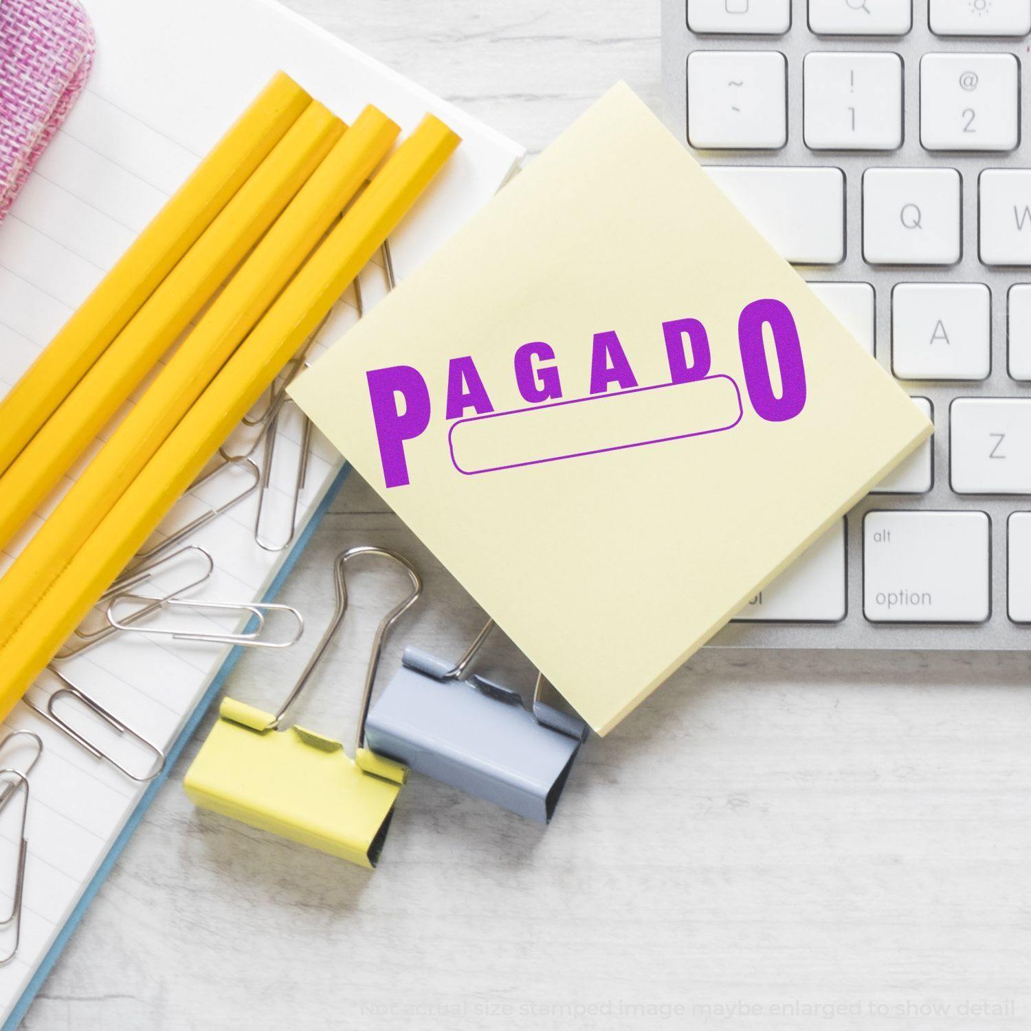 Large Self Inking Pagado with Box Stamp on a desk with pencils, paper clips, binder clips, and a keyboard in the background.