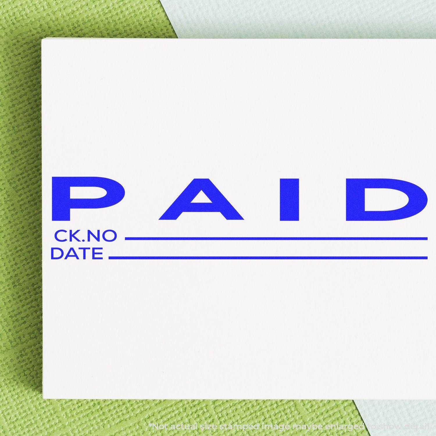 Large Paid with Ck No Rubber Stamp in blue ink on white paper, with lines for check number and date, placed on a green textured surface.