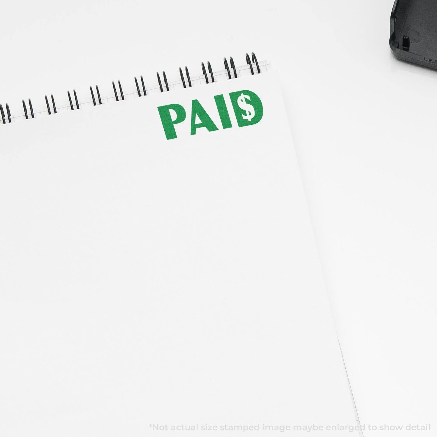 Notebook page stamped with 'PAID' in green ink, featuring a dollar sign, using a rubber stamp.